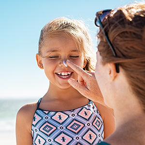 Mom putting Noz colorful sunscreen on smiling daughter.